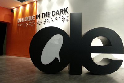 Photo of the lobby of the Dialogue inthe Dark, Hong Kong: the walls in orange and white, and with a large sculpture of the letters d and e