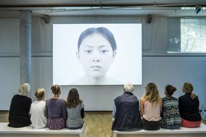 Foto der ersten Station in der Dialog mit der Zeit-Ausstellung, an der ein Video gezeigt wird, das den Alterungsprozess des Gesichtes einer Frau vom Kindes- bis ins hohen Alter simuliert.