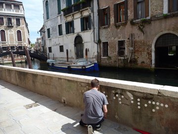 Photo of The Blind attaching a braille grafitti to a Venice wall next to a canal.