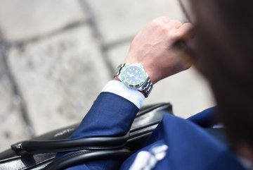 Photo over the shoulder of a man in a suit looking at  his watch.