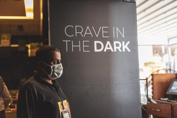 Foto eines Guides, der neben einer Wand steht auf der der Schriftzug "Crave in the Dark" zu lesen ist.