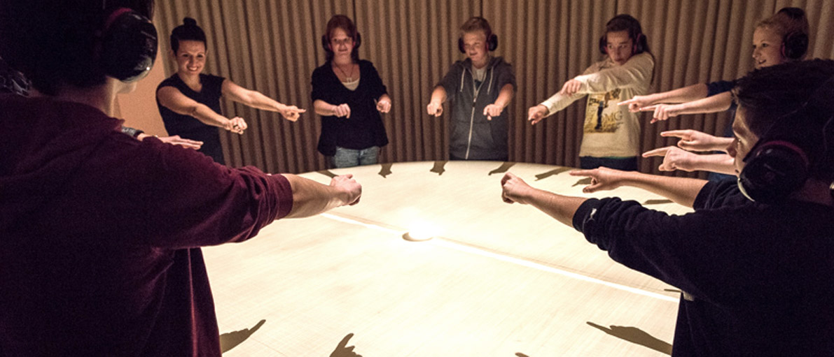 Bild einer Dialog im Stillen Gruppe im Raum Tanz der Hände, wo das Schattenspiel der Hände auf einen großen runden Tisch projiziert wird.